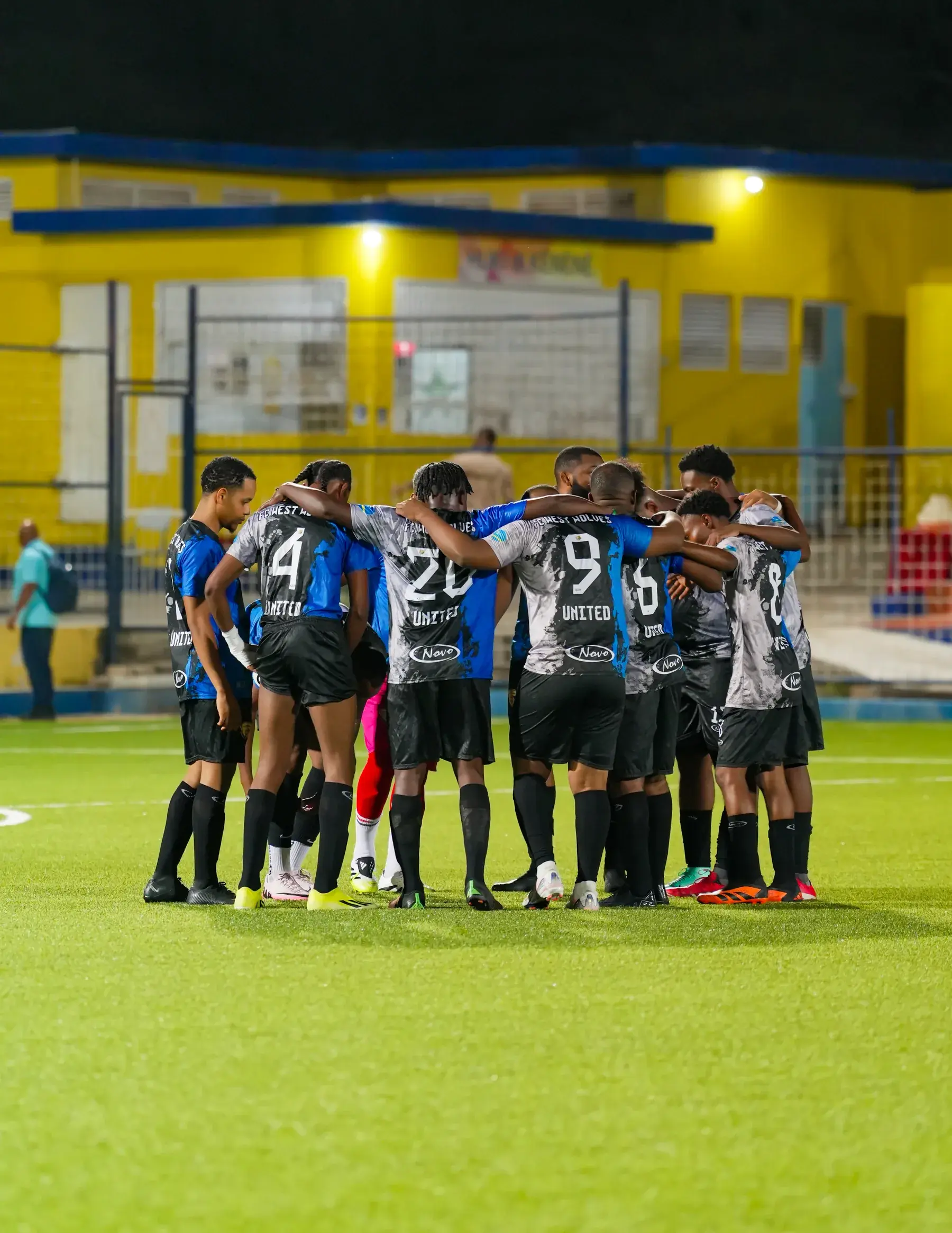 West Wolves United players with arms around one another in a huddle on the pitch.