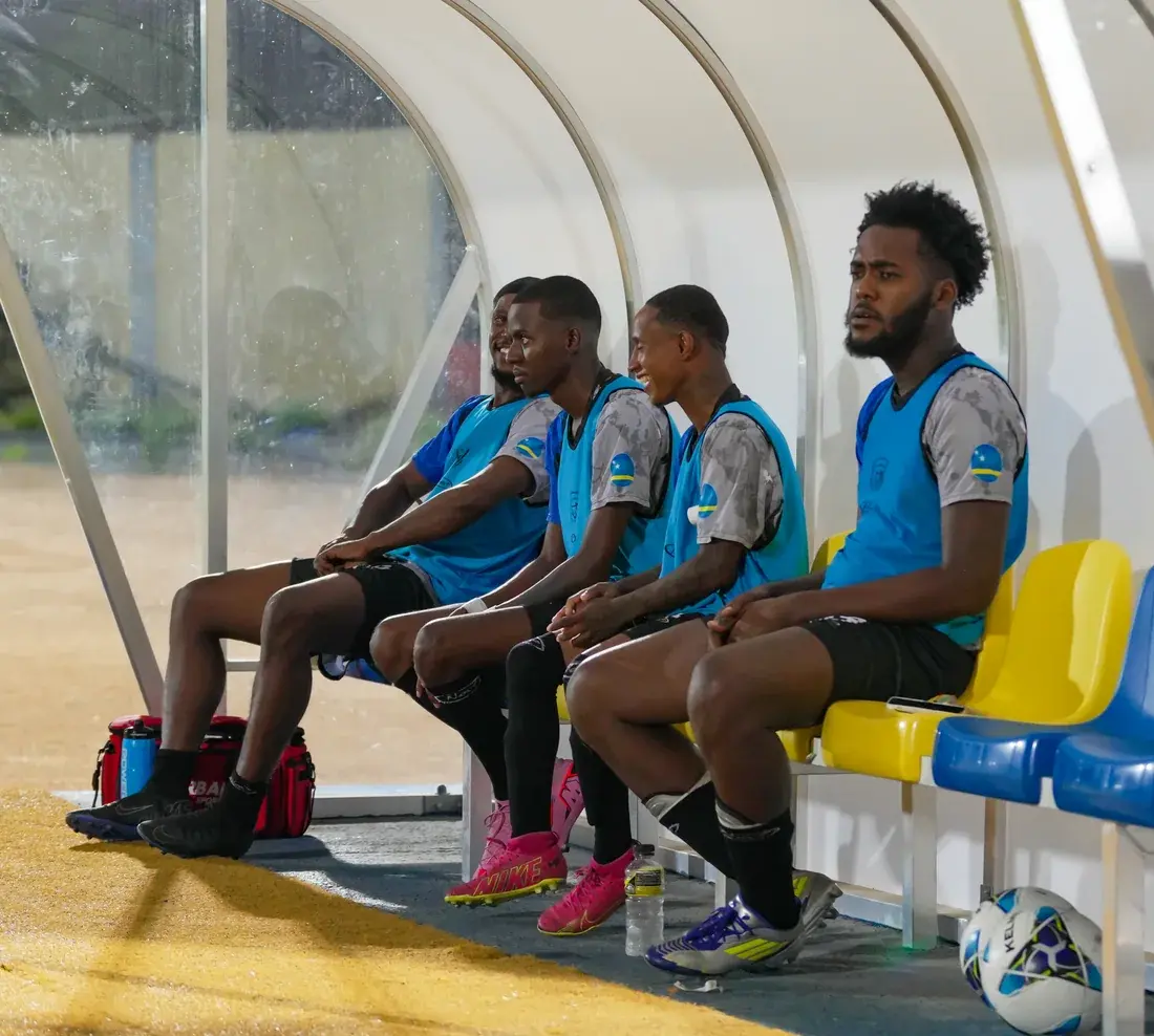 West Wolves United teammates in blue bibs sitting together in the dugout.