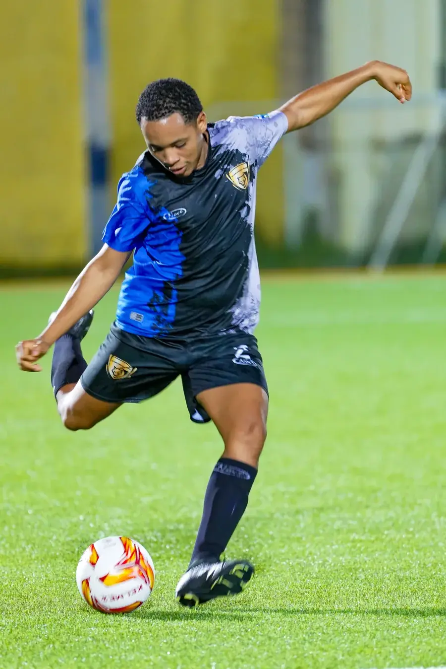 A West Wolves United player striking the ball in blue, black and grey kit.